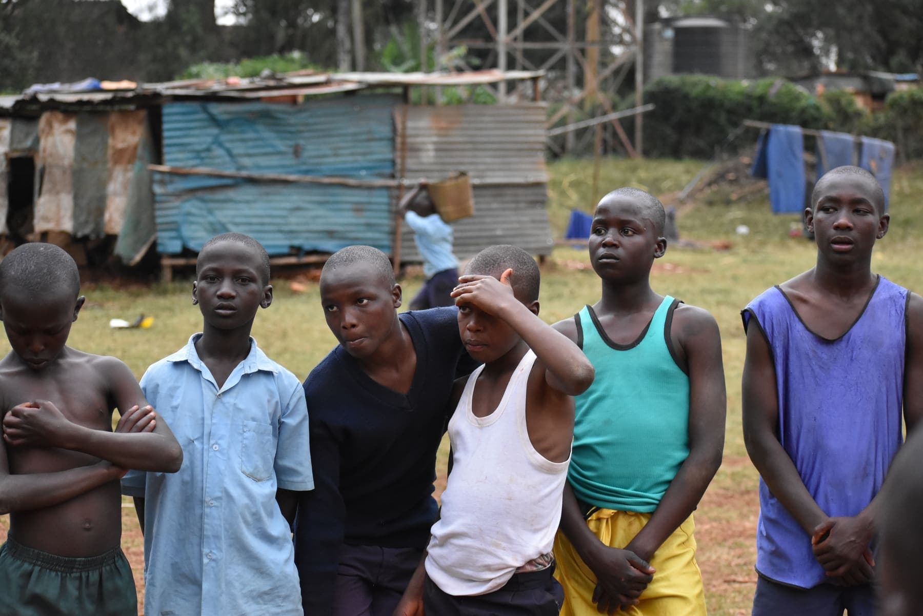 Players resting between drills beside corrugated-iron buildings, one shielding his eyes from the sun.