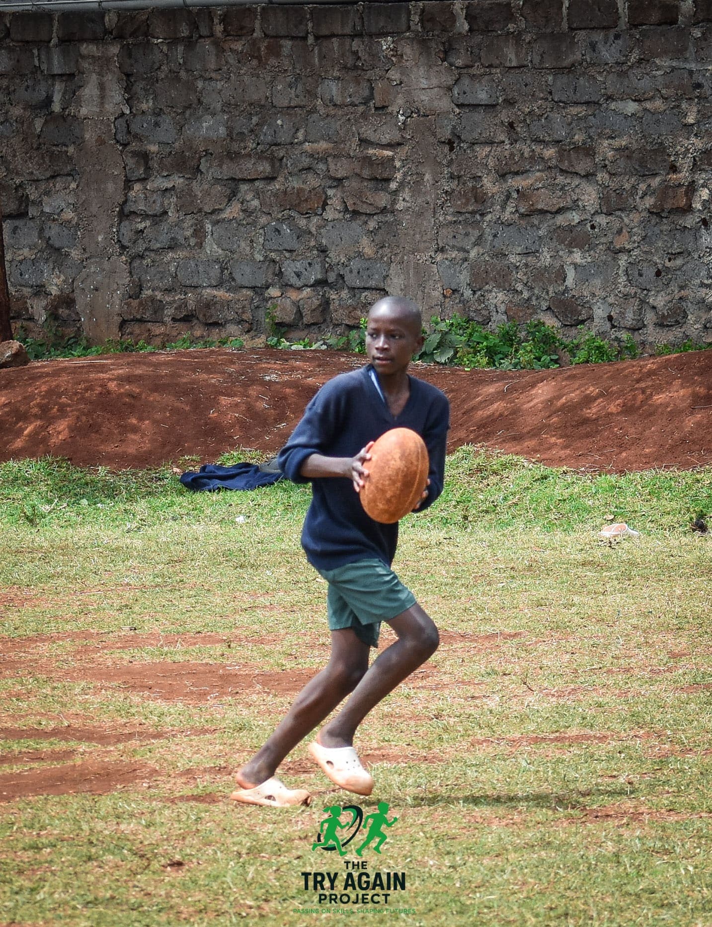 A young player running with the ball held in both hands, driving forward across the grass.