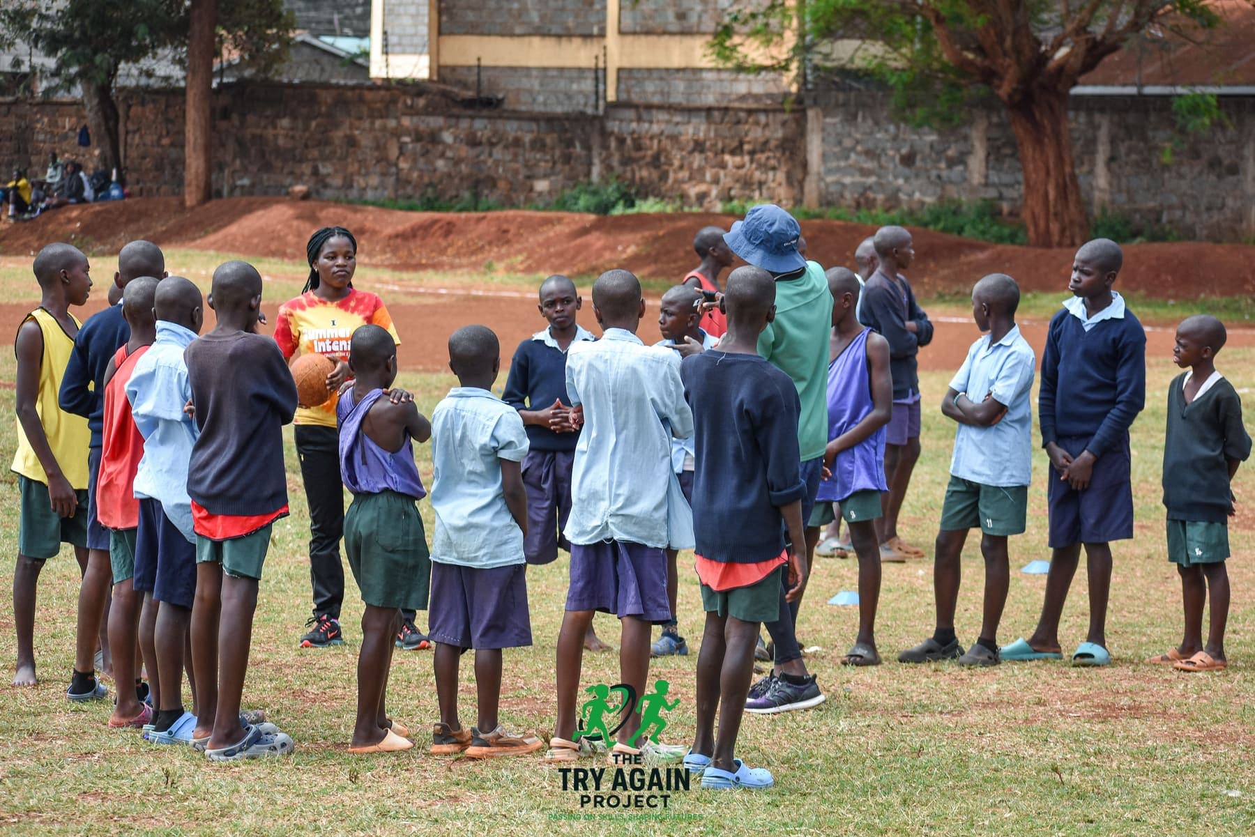 A coach holding a rugby ball and talking to a semicircle of players gathered around her before training begins.