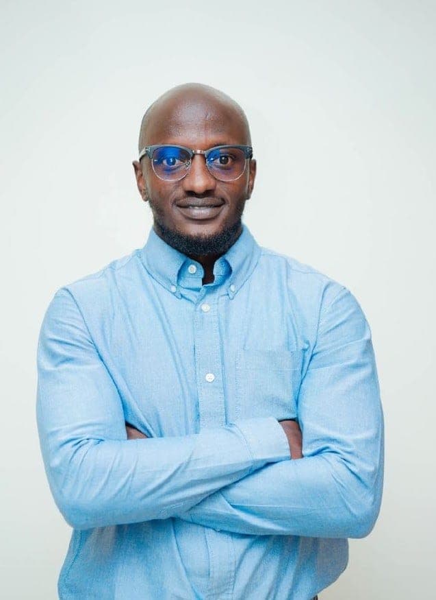 Fabian Kowido with his arms folded in a light blue shirt and glasses, against a white backdrop.